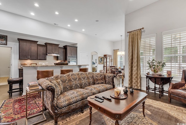 living area featuring recessed lighting, wood finished floors, a high ceiling, arched walkways, and baseboards