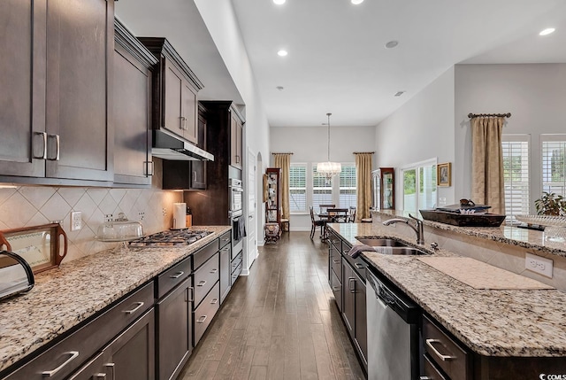 kitchen with a sink, stainless steel appliances, light stone countertops, a towering ceiling, and recessed lighting