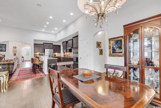 dining space featuring arched walkways, wood finished floors, a towering ceiling, recessed lighting, and a chandelier