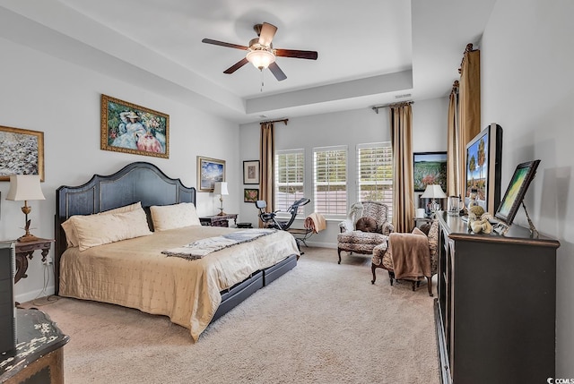 bedroom with a raised ceiling, ceiling fan, and light colored carpet