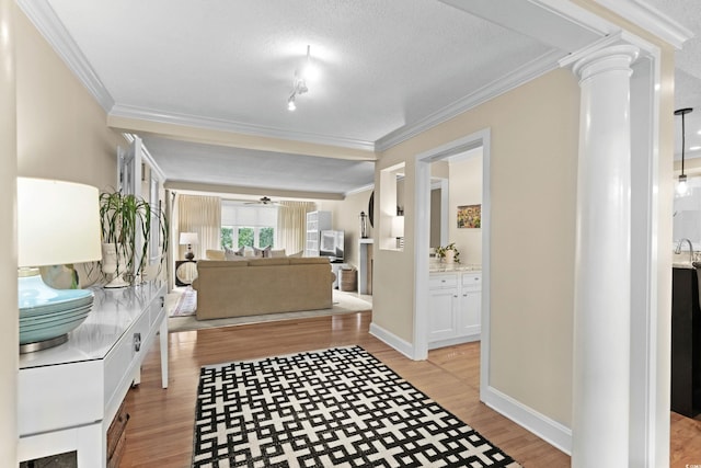 hallway featuring a textured ceiling, light hardwood / wood-style flooring, crown molding, and ornate columns