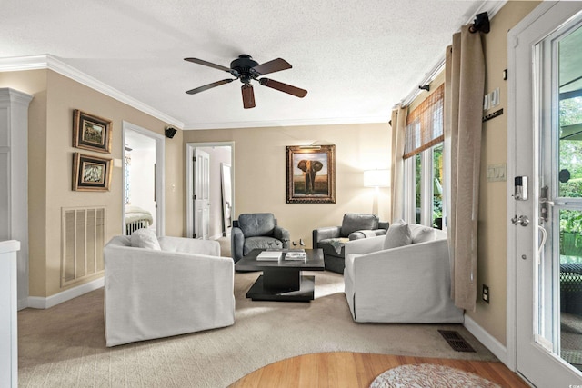 living room featuring ceiling fan, light wood-type flooring, ornamental molding, and a textured ceiling