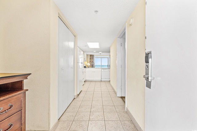 corridor featuring a textured ceiling, light tile patterned floors, and a skylight