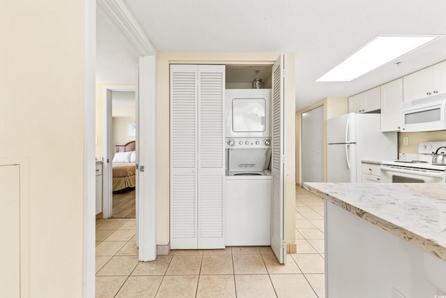 kitchen featuring stacked washing maching and dryer, white cabinetry, white appliances, light stone countertops, and light tile patterned floors