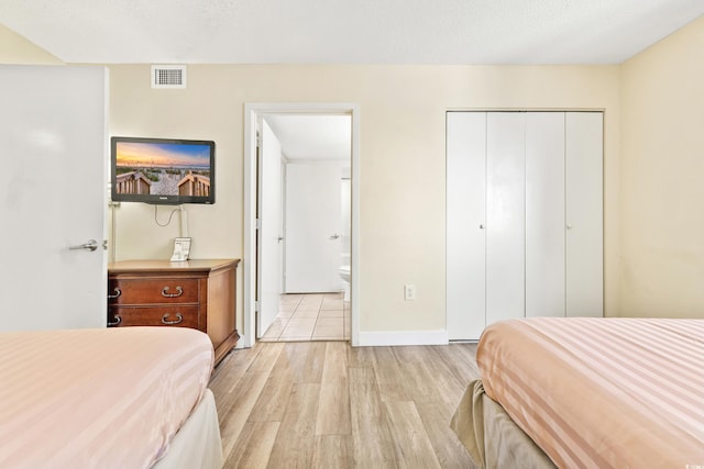 bedroom featuring light wood-type flooring, a textured ceiling, connected bathroom, and a closet