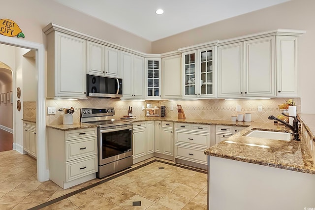 kitchen with stainless steel appliances, white cabinetry, sink, tasteful backsplash, and light stone countertops