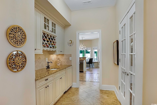 bar featuring cream cabinets, light stone counters, backsplash, light tile patterned floors, and sink