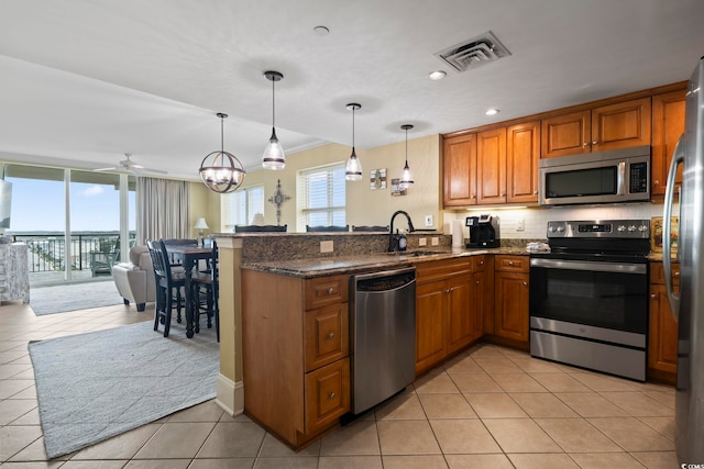 kitchen with sink, kitchen peninsula, decorative light fixtures, appliances with stainless steel finishes, and dark stone countertops