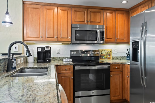 kitchen with pendant lighting, appliances with stainless steel finishes, sink, and light stone countertops