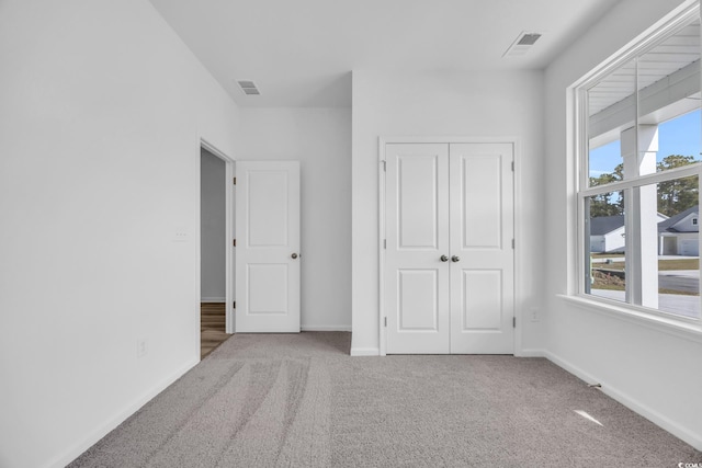 unfurnished bedroom featuring multiple windows, light carpet, and a closet