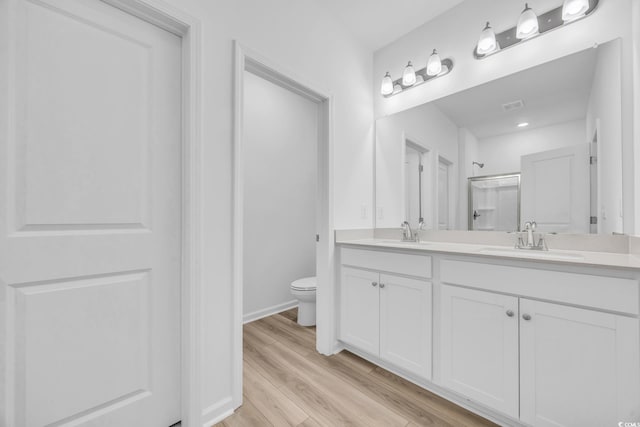 bathroom featuring wood-type flooring, vanity, toilet, and a shower with shower door