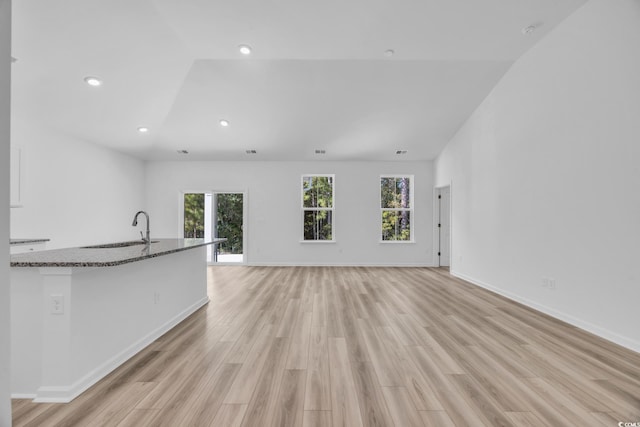 unfurnished living room featuring sink, light wood-type flooring, and lofted ceiling