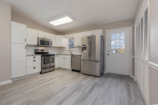 kitchen with decorative backsplash, sink, white cabinetry, appliances with stainless steel finishes, and light hardwood / wood-style floors