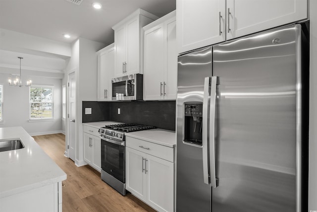 kitchen with light wood-type flooring, white cabinets, hanging light fixtures, backsplash, and appliances with stainless steel finishes