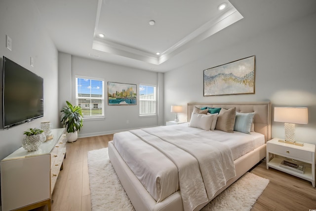 bedroom with light wood-type flooring and a tray ceiling