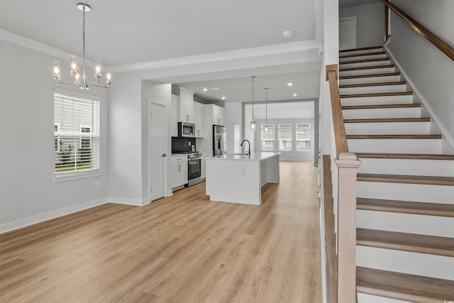 interior space with appliances with stainless steel finishes, a center island with sink, white cabinetry, and pendant lighting