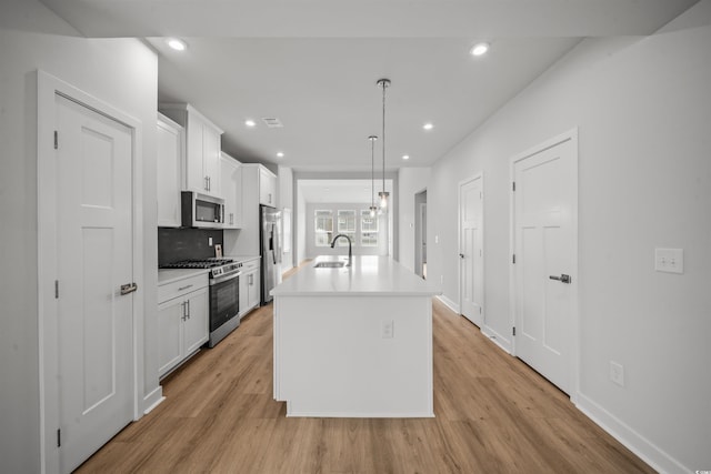 kitchen with light wood-type flooring, an island with sink, stainless steel appliances, and hanging light fixtures