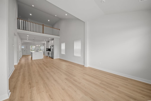 unfurnished living room with light wood-type flooring and high vaulted ceiling