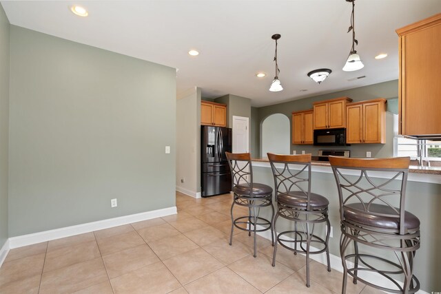 kitchen with kitchen peninsula, hanging light fixtures, light tile patterned floors, black appliances, and a breakfast bar area