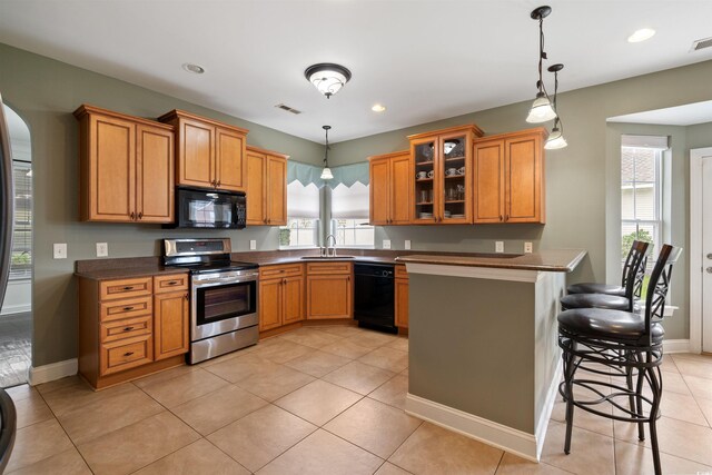 kitchen with hanging light fixtures, light tile patterned floors, black appliances, a kitchen breakfast bar, and sink