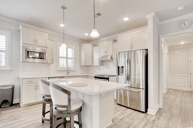 kitchen featuring a center island, ornamental molding, appliances with stainless steel finishes, pendant lighting, and white cabinets