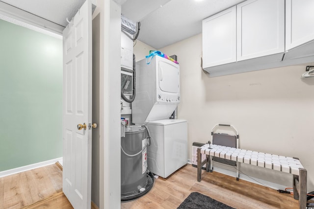 washroom with electric water heater, light wood-type flooring, cabinets, stacked washer / drying machine, and a textured ceiling