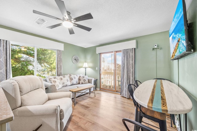 living room featuring ceiling fan, a textured ceiling, and light hardwood / wood-style floors