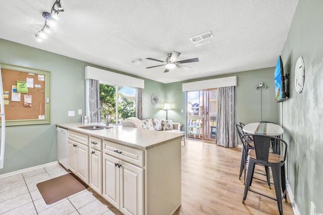 kitchen with light wood-type flooring, ceiling fan, sink, white dishwasher, and a textured ceiling