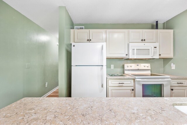 kitchen with a textured ceiling, light stone counters, white appliances, and white cabinets