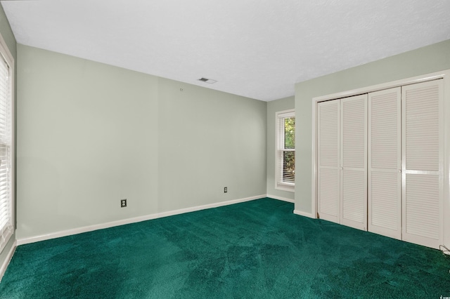 unfurnished bedroom with baseboards, a closet, dark colored carpet, and visible vents