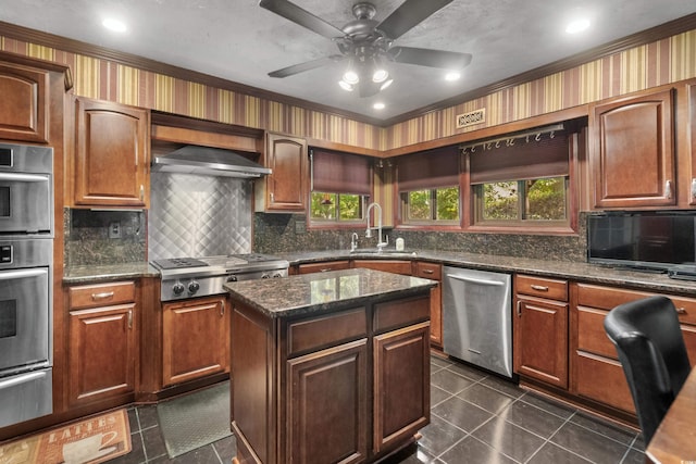 kitchen featuring wall chimney range hood, a sink, stainless steel appliances, backsplash, and a warming drawer