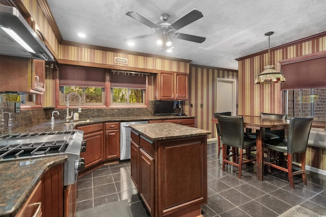 kitchen featuring stainless steel dishwasher, ornamental molding, wall chimney exhaust hood, a sink, and ceiling fan with notable chandelier
