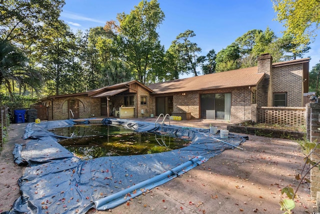 rear view of property with brick siding, a chimney, a fenced in pool, and a patio