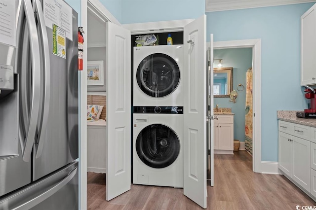 washroom featuring ornamental molding, light hardwood / wood-style flooring, and stacked washer and dryer