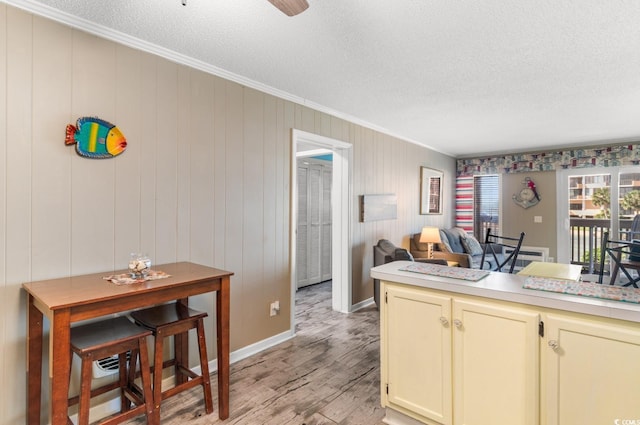 kitchen with wood walls, cream cabinetry, light wood-type flooring, a textured ceiling, and crown molding