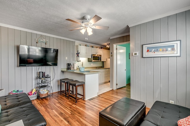 living room featuring light hardwood / wood-style floors, ceiling fan, ornamental molding, and wood walls