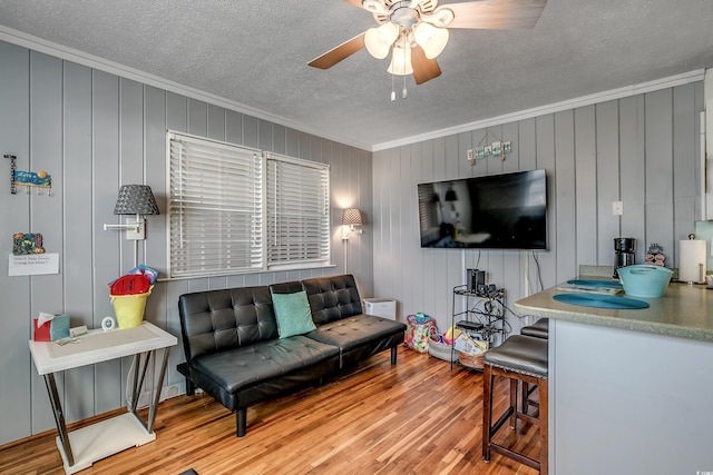 living room with a textured ceiling, light hardwood / wood-style flooring, ceiling fan, and crown molding