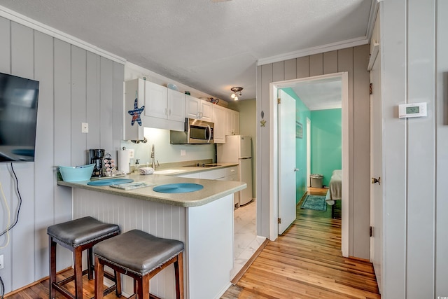 kitchen with white cabinets, a kitchen breakfast bar, a textured ceiling, white fridge, and light hardwood / wood-style floors