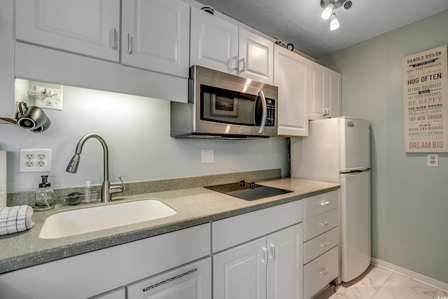 kitchen featuring refrigerator, white cabinetry, sink, and black electric cooktop