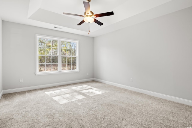 carpeted empty room featuring ceiling fan, a tray ceiling, visible vents, and baseboards