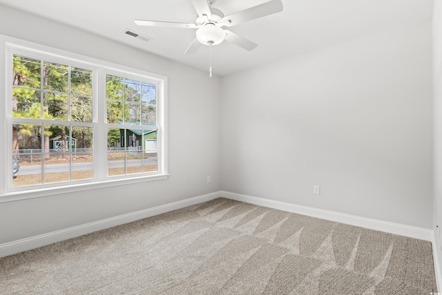 empty room with a ceiling fan, light colored carpet, visible vents, and baseboards