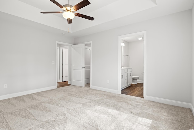 unfurnished bedroom featuring a tray ceiling, ensuite bath, carpet flooring, and baseboards