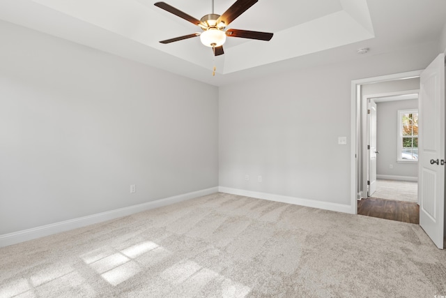 empty room with carpet floors, a tray ceiling, ceiling fan, and baseboards