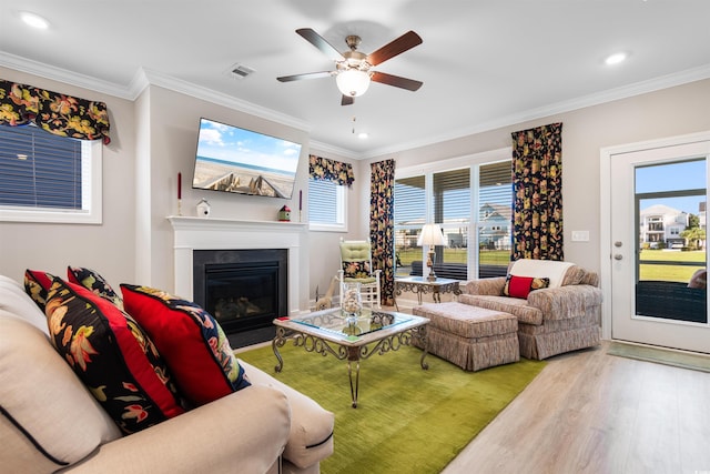 living room with light wood-type flooring, crown molding, ceiling fan, and a wealth of natural light