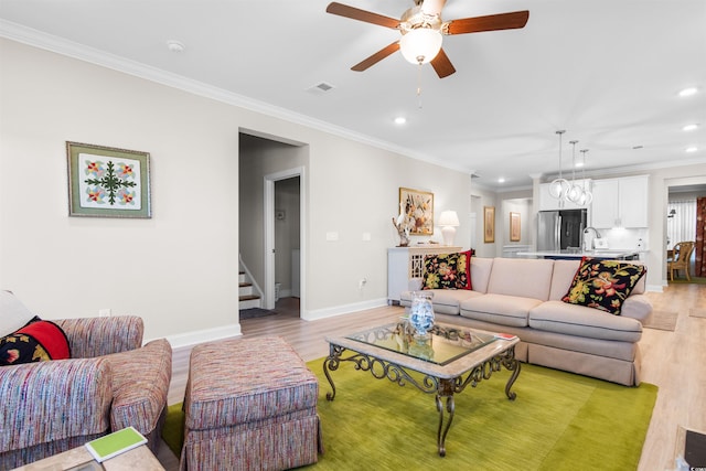 living room featuring ceiling fan with notable chandelier, light wood-type flooring, sink, and crown molding