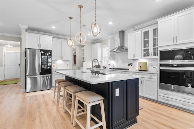 kitchen featuring a kitchen breakfast bar, an island with sink, white cabinets, stainless steel appliances, and wall chimney range hood