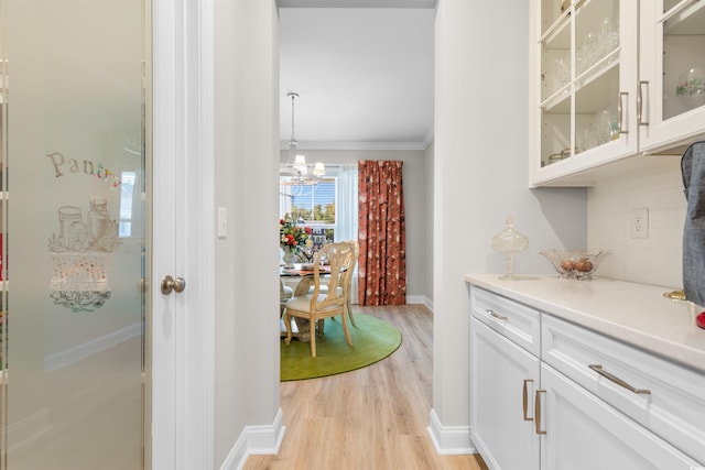 bar featuring decorative backsplash, light hardwood / wood-style floors, white cabinetry, crown molding, and decorative light fixtures