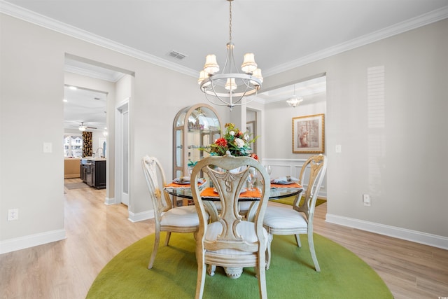 dining area featuring light wood-type flooring, ceiling fan with notable chandelier, and crown molding