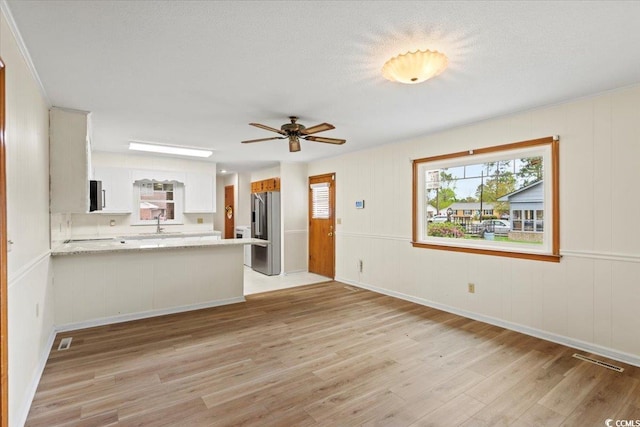 unfurnished living room with light wood-type flooring, ceiling fan, sink, and a textured ceiling