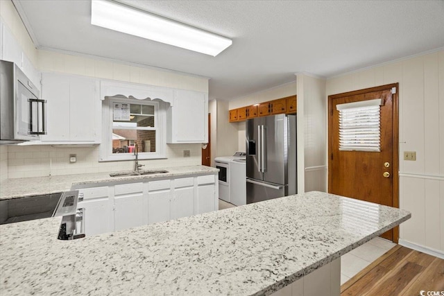 kitchen featuring washer / dryer, sink, white cabinetry, light hardwood / wood-style flooring, and appliances with stainless steel finishes